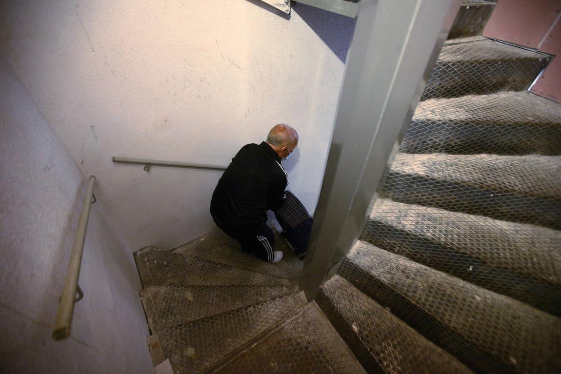 Un anciano sube con el carro de la compra por la misma escalera metálica. 