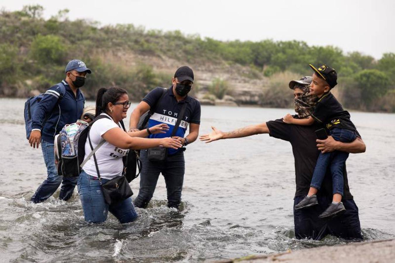 Una mujer intenta coger la mano de un compañero para poder cruzar el río. 
