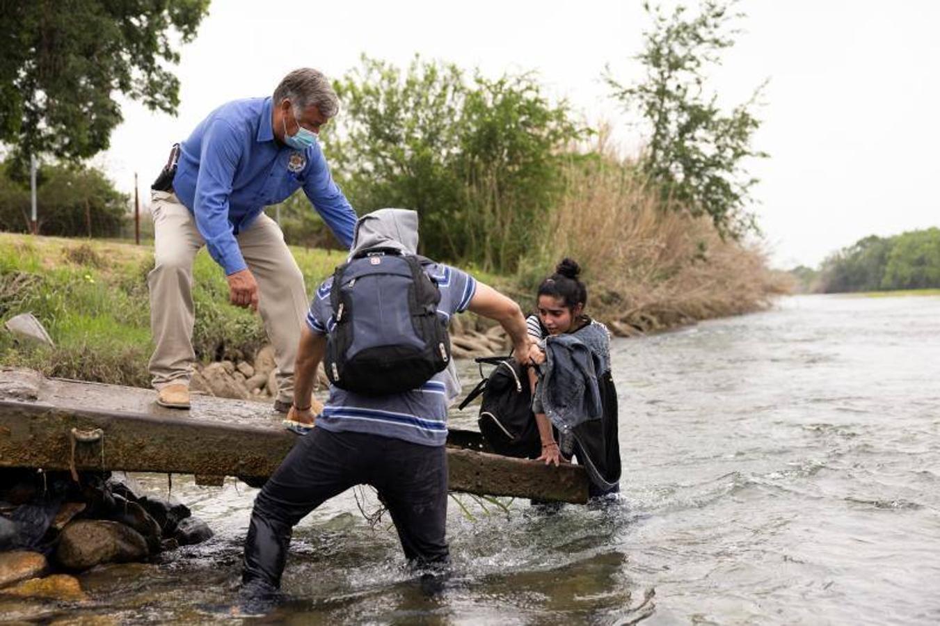 Un agente y un inmigrante ayudan a una joven a salir del agua. 