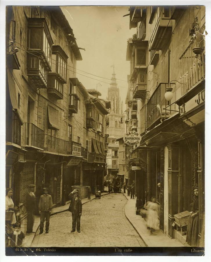 Tramo bajo de la calle del Comercio en una postal de Linares hacia 1917. Sobre un pavimento ya adoquinado posan varios transeúntes. En la acera izquierda la «Antigua Funeraria. Librería, cerería y objetos de escritorio de M. San Román». 