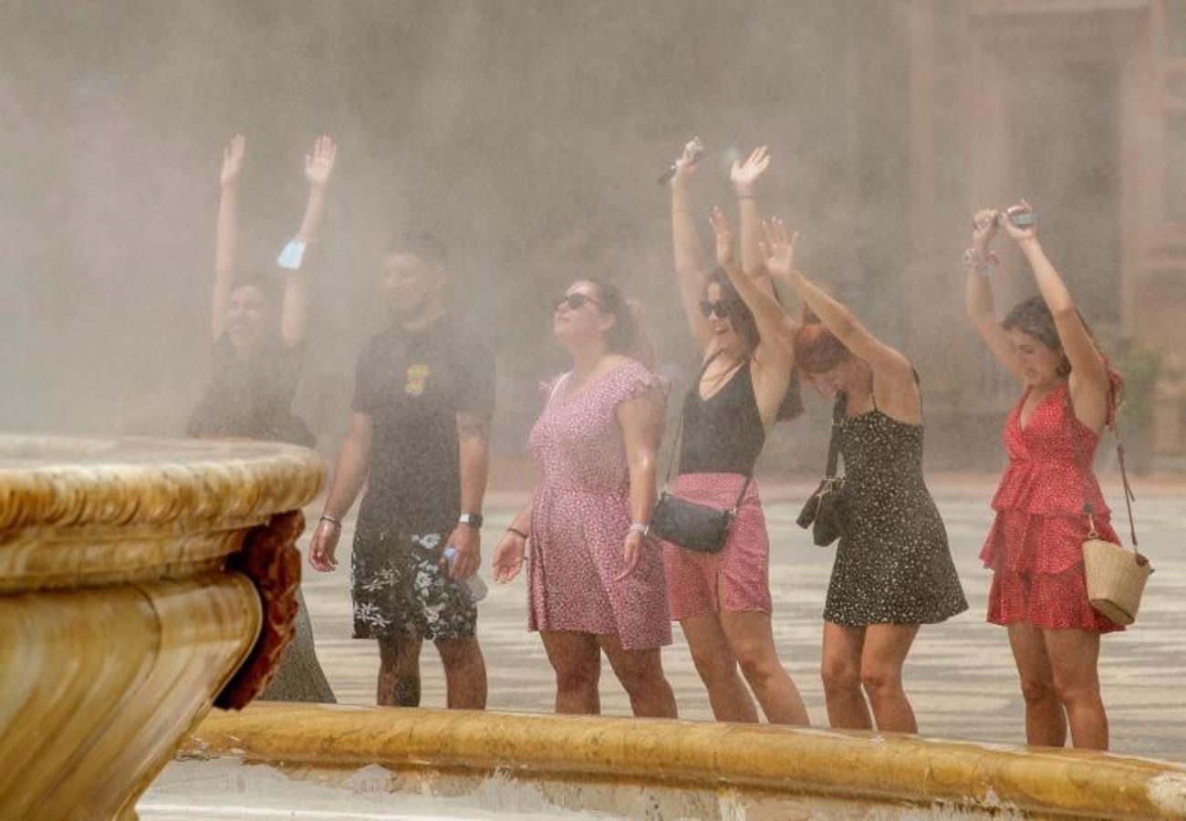 Unos turistas se refrescan con el agua que desprende la fuente de la Plaza de España en Sevilla. 