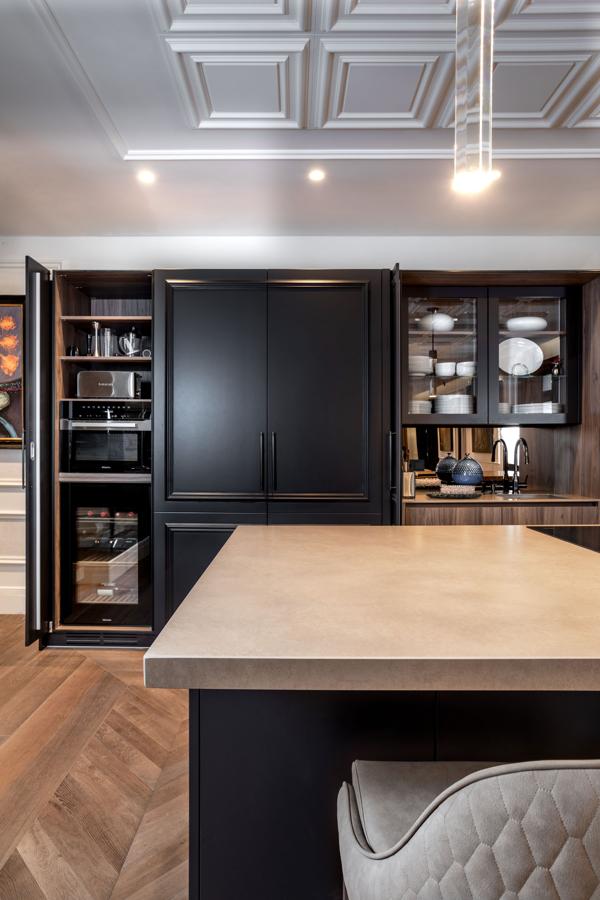 Exclusividad en el barrio de Salamanca. La cocina cuenta con gabinetes en tonos negros, electrodomésticos de alta gama y hasta una nevera para vinos. Destaca, también, su isla con barra de desayuno y unas cómodas butacas que invitan a disfrutar del primer café de la mañana en compañía de la familia.