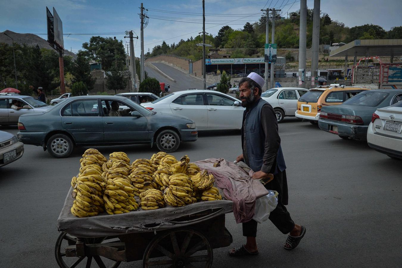 Un vendedor de frutas afgano empuja su carrito lleno de plátanos a lo largo de una carretera muy transitada en Kabul. 