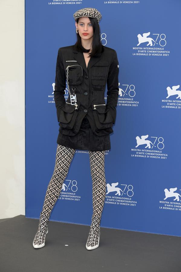 Milena Smit, en el Festival de cine de Venecia 2021. Junto a Pe, en la alfombra de la presentación de 'Madrid Paralelas', la actriz ha debutado en el Festival compartiendo reparto en la cinta de Pedro Almodóvar. En esta ocasión, la actriz ha optado por  un traje negro de estilo militar formado por chaqueta de doble bolsillo y falda de Marine Serre. Un estilismo combinado con medias estampadas de estilo retro a juego con los botines calcetín y una gorra de la misma firma.