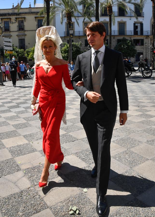 Miriam Lapique y Carlos Cortina. La madre del novio ejerció de madrina con un elegante diseño midi en rojo con escote Bardot de líneas rectas y un nudo drapeado que comenzaba en la cintura y hacía que la falda con abertura se presentase cruzada. Añadió una mantilla y salones rojos.