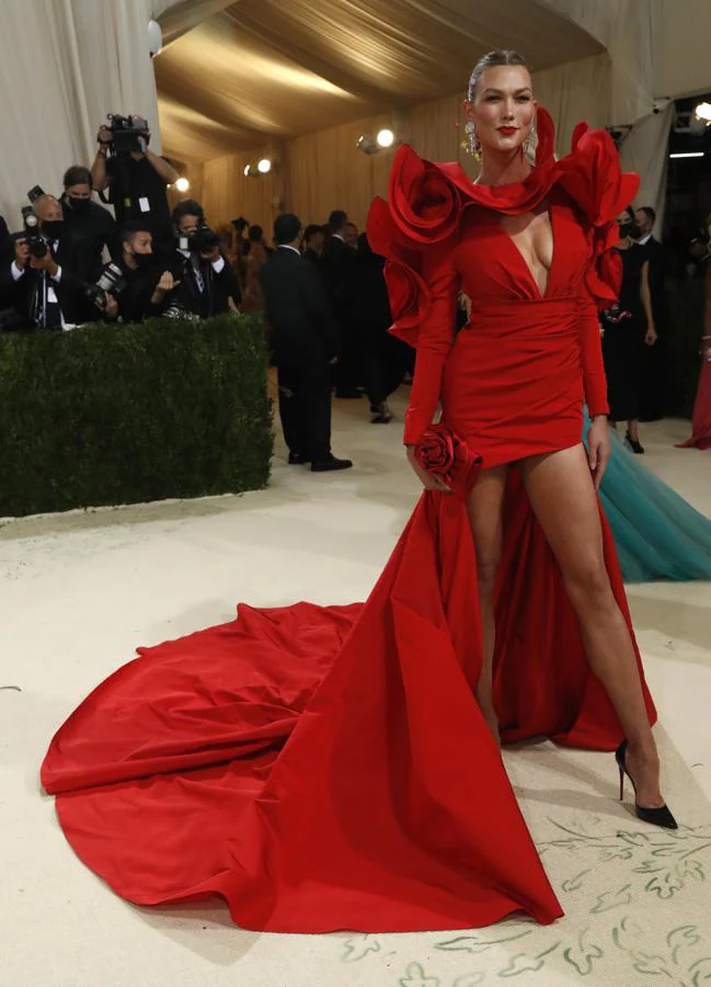 Karlie Kloss - Alfombra roja de la Gala MET 2021. Fiel a Carolina Herrera, deslumbró con un vestido rojo cuyo cuello simulaba los pétalos de una flor -igual que su bolso- y que en la falda presentaba una asimetría con la parte delantera más corta y una gran cola por detrás.