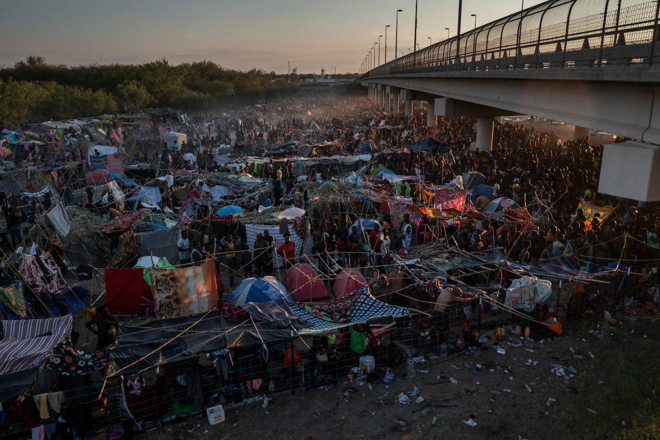 Varios migrantes se refugian a lo largo del Puente Internacional Del Río al atardecer mientras esperan a conocer su destino ​​después de cruzar el Río Grande. 