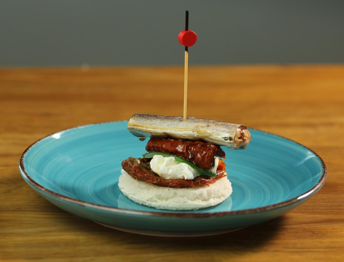 Pintxo de aguja con tomate seco. Puedes preparar este entrante con una lata de agujas Rianxeira en AOVE, pan integral de molde, albahaca, tomate seco y queso crema. A la hora de emplatar, échale imaginación y arte.