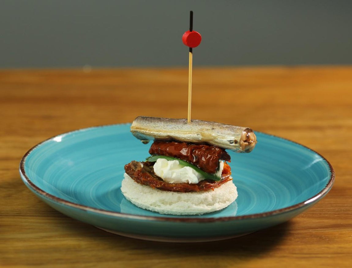 Pintxo de aguja con tomate seco. Puedes preparar este entrante con una lata de agujas Rianxeira en AOVE, pan integral de molde, albahaca, tomate seco y queso crema. A la hora de emplatar, échale imaginación y arte.