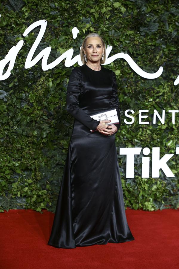 Kristin Scott Thomas - Alfombra roja de los British Fashion Awards. Llevó un diseño negro de seda con cuello a la caja y manga larga que se ajustaba a su figura en la parte superior y cuya falda acampanada se ceñía a la cintura, estilizándola.