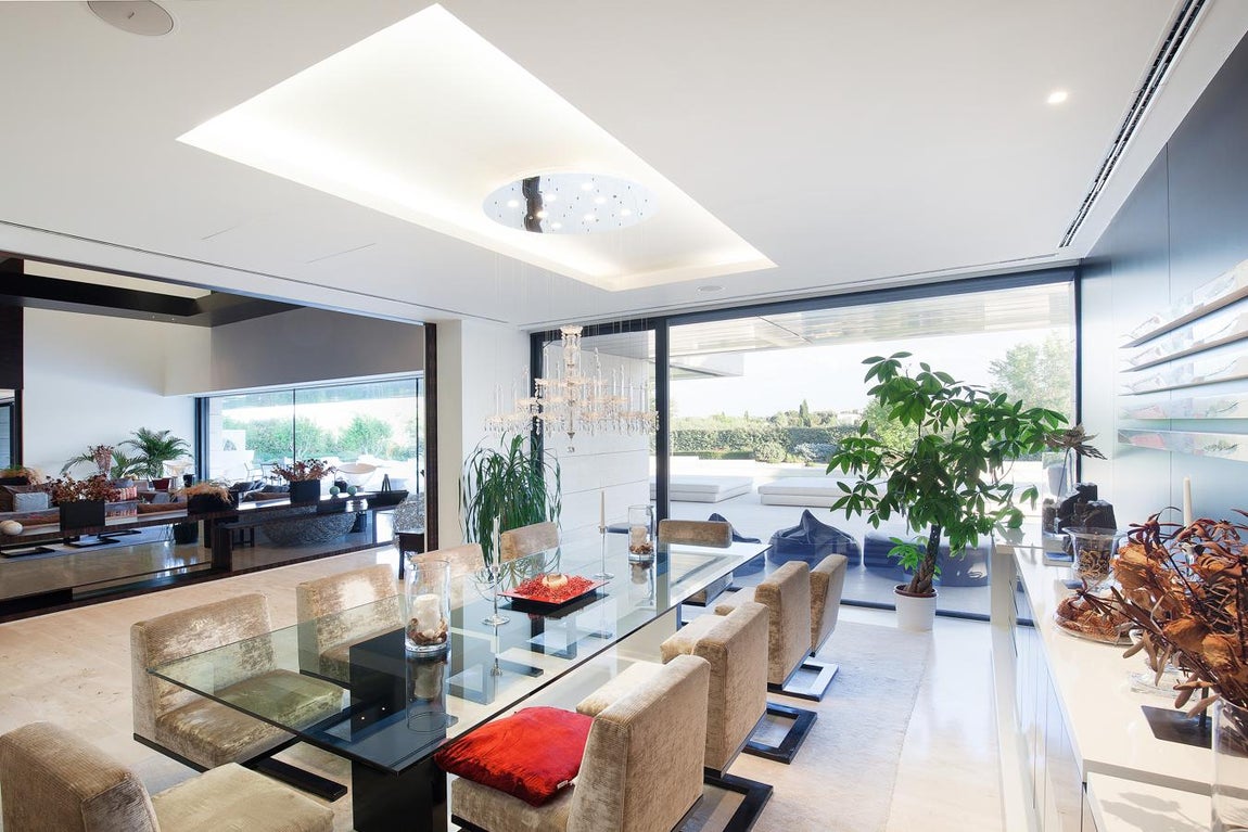 La exclusiva propiedad de La Moraleja para vivir rodeado de lujos. La zona del comedor hace del vidrio el material predominante con una mesa de diez comensales y una elegante lámpara de araña que lo convierten en un espacio ideal para recibir invitados.