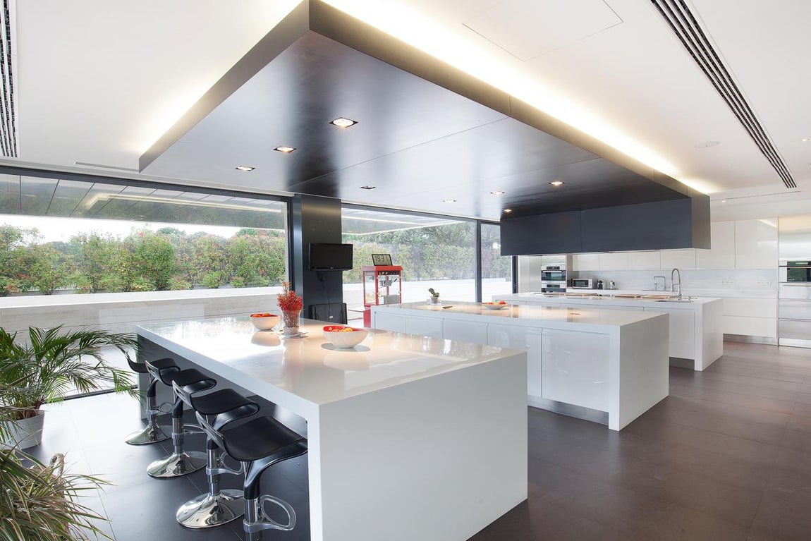 La exclusiva propiedad de La Moraleja para vivir rodeado de lujos. La cocina es muy amplia y comunica con el jardín a través de una puerta corredera acristalada. Posee electrodomésticos de última generación y dos islas centrales, una de las cuáles sirve como mesa de comedor.