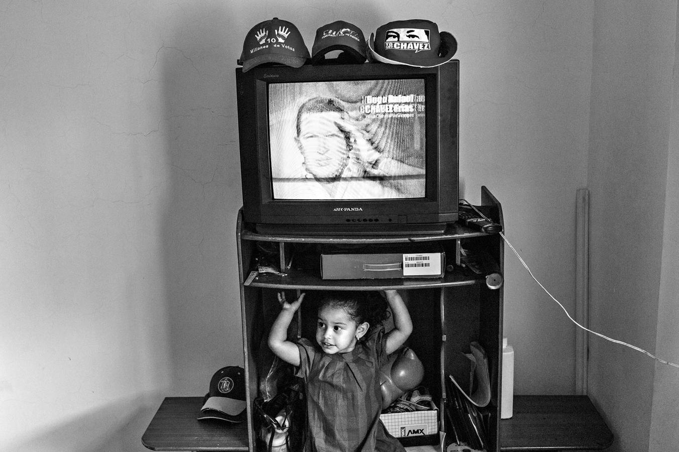 La hija de un miliciano bolivariano juega junto al televisor dentro de una casa donada del Plan Vivienda del régimen chavista. 