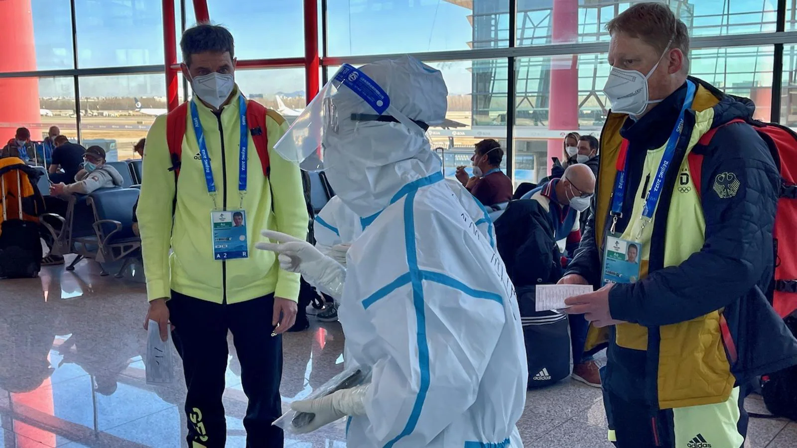 En la terminal 3 del aeropuerto de Pekín, operarios pertrechados con trajes especiales de protección dan la bienvenida a los deportistas, miembros de comités olímpicos y periodistas que llegan a China para los Juegos. 