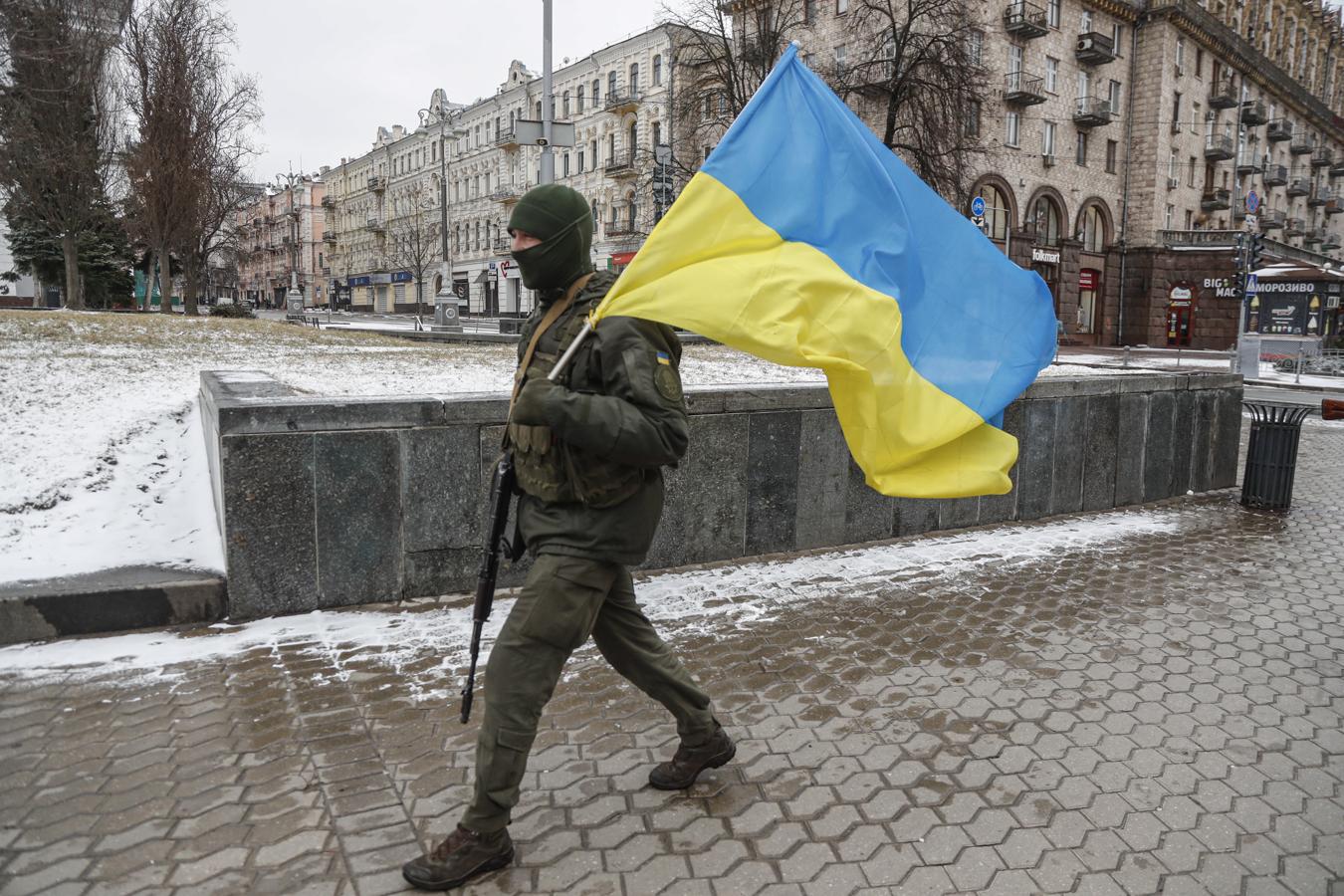 Un soldado ucraniano camina con una bandera de su país en Kiev. 