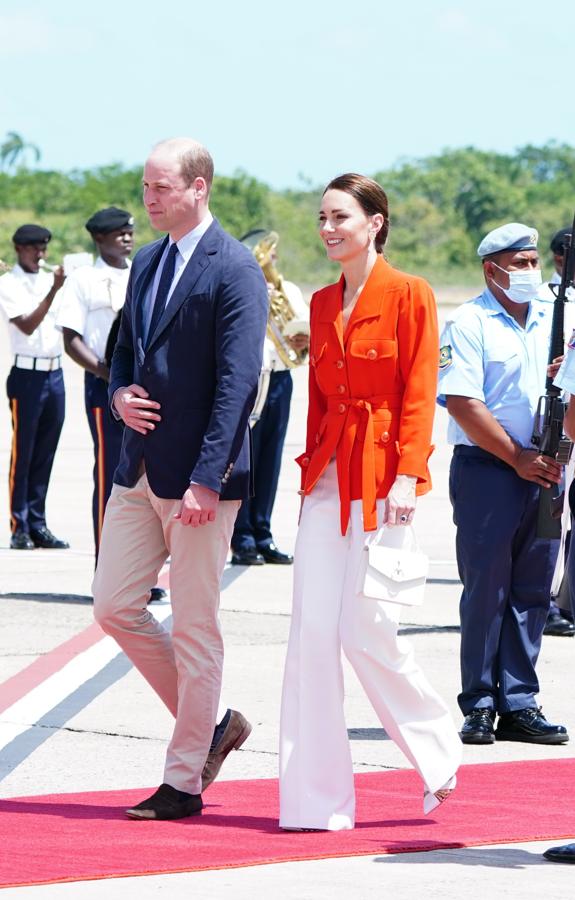 Los looks de Kate Middleton en su gira por el Caribe. Para viajar de Belice a Jamaica apostó por uno de sus outfits más elegantes compuesto por una camisa vintage de Yves Saint Laurent anaranjada con bolsillos XXL y un cinturón dle mismo tejido que combinó con unos pantalones palazzo blancos, minibolso a juego de Mulberry, pendientes que podría haber adquirido en el país y unos stilettos con detalles metalizados de Aquazzura.