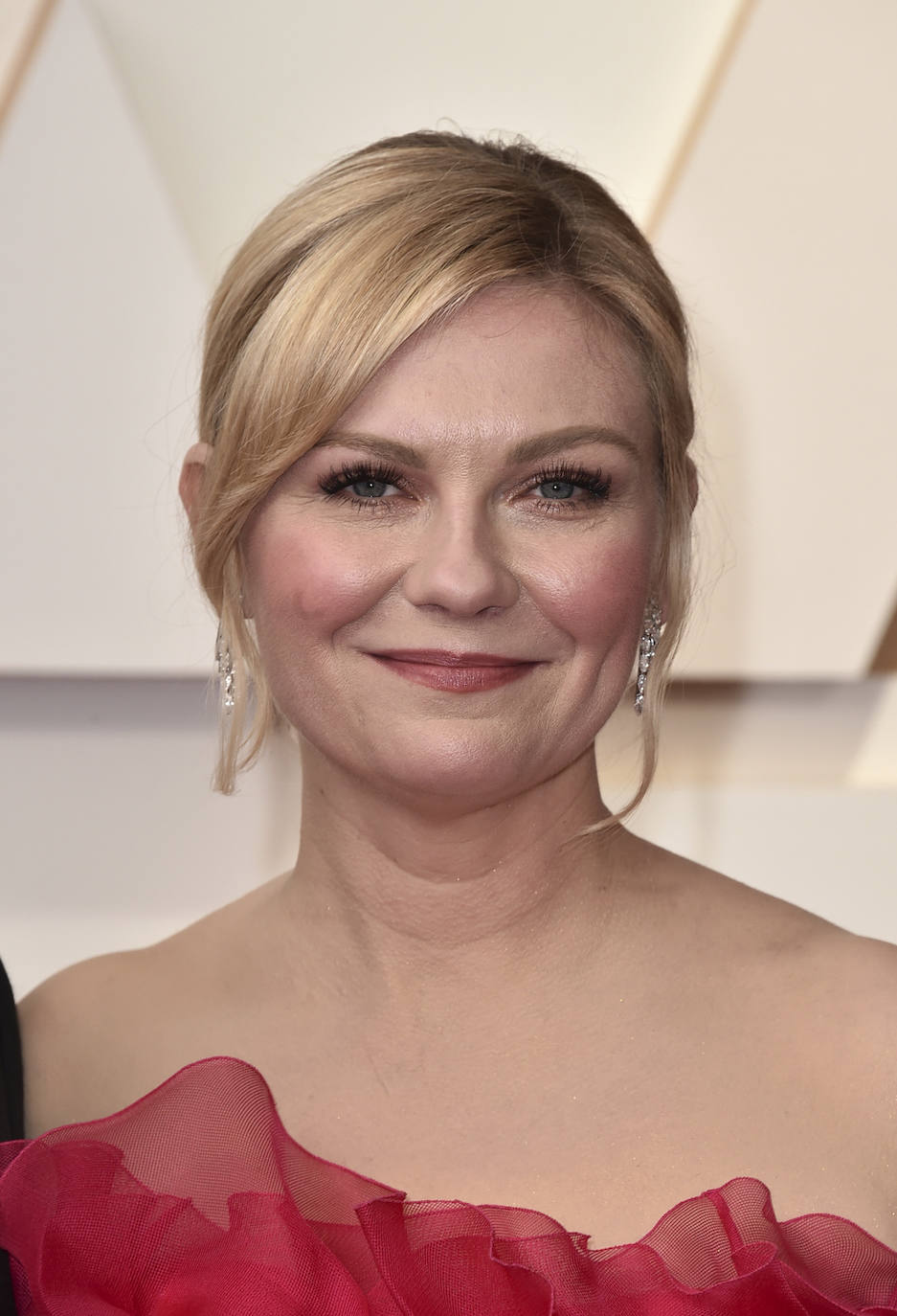 Kirsten Dunst con un beauty look clásico en los  Oscar 2022. La actriz se ha decantado por un moño, con flequillo lateral y mechones sueltos y un maquillaje nude con los labios frambuesa, a juego con su vestido.