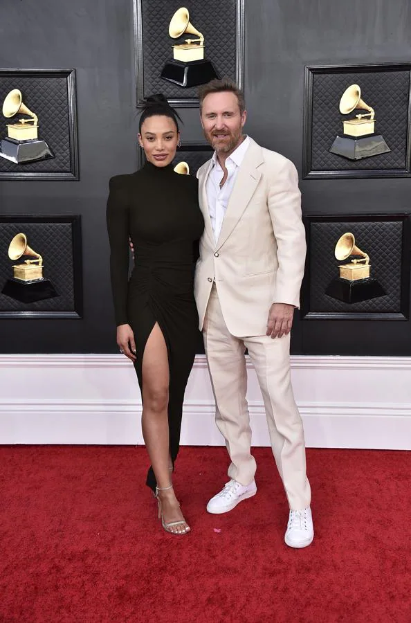 David Guetta y Jessica Ledon - Alfombra roja de los Grammy 2022. El DJ se decantó por un traje blanco y su pareja hizo lo contrario con un ajustado vestido con una gran abertura lateral.