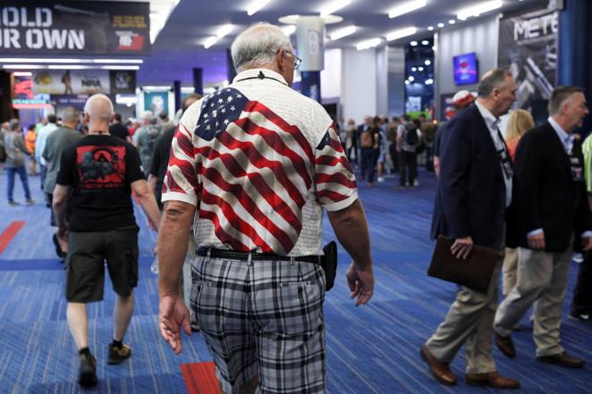 Un hombre con un polo con la bandera de Estados Unidos pasea por la Convención Nacional del Rifle que se celebra en Houston (Texas).