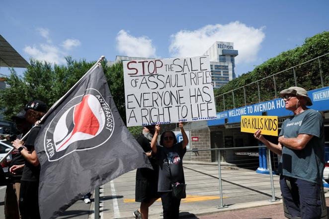 Una bandera de activistas 'antifascistas' y otra en la que se puede leer: «Detened la venta de rifles de asalto, todo el mundo tiene derecho a la vida». Los manifestantes se han reunido en la puerta de la Convención Nacional del Rifle que se celebra en Houston (Texas).