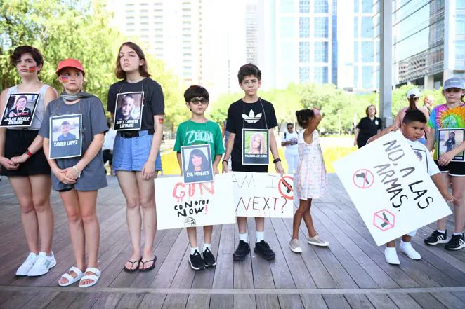 Varios niños sostienen pancartas y fotografías de víctimas del tiroteo de Uvalde a las puertas de la Convención Nacional del Rifle.