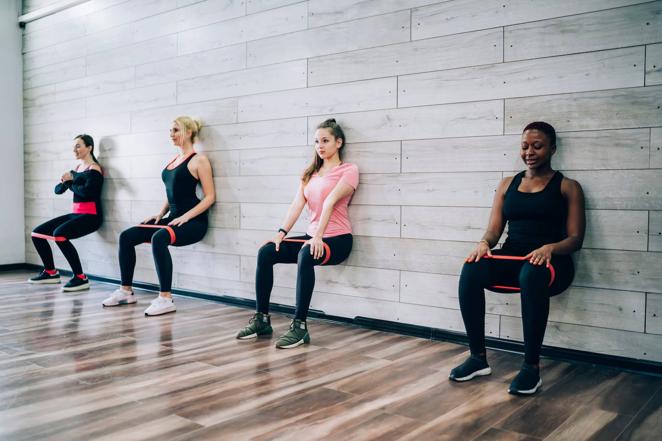 Sentadilla isométrica. La sentadilla isométrica se ejecuta colocándose en posición de sentadilla, con las piernas en un ángulo de 90 grados y la espalda apoyada sobre una pared. Entonces aguanta en esta posición durante el máximo tiempo posible. Se recomienda hacer series de 1 minuto. La banda irá colocada por encima de las rodillas y, si quieres aumentar la intensidad del ejercicio, cuando estés en posición de sentadilla abre y cierra las piernas ligeramente.