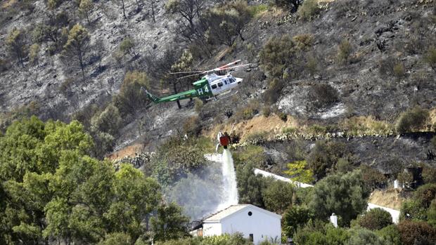 Un helicóptero arroja agua sobre una vivienda tras un incendio forestal