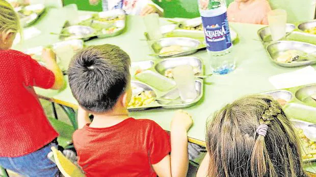 Niños con sus bandejas de almuerzo sobre las mesas del comedor escolar