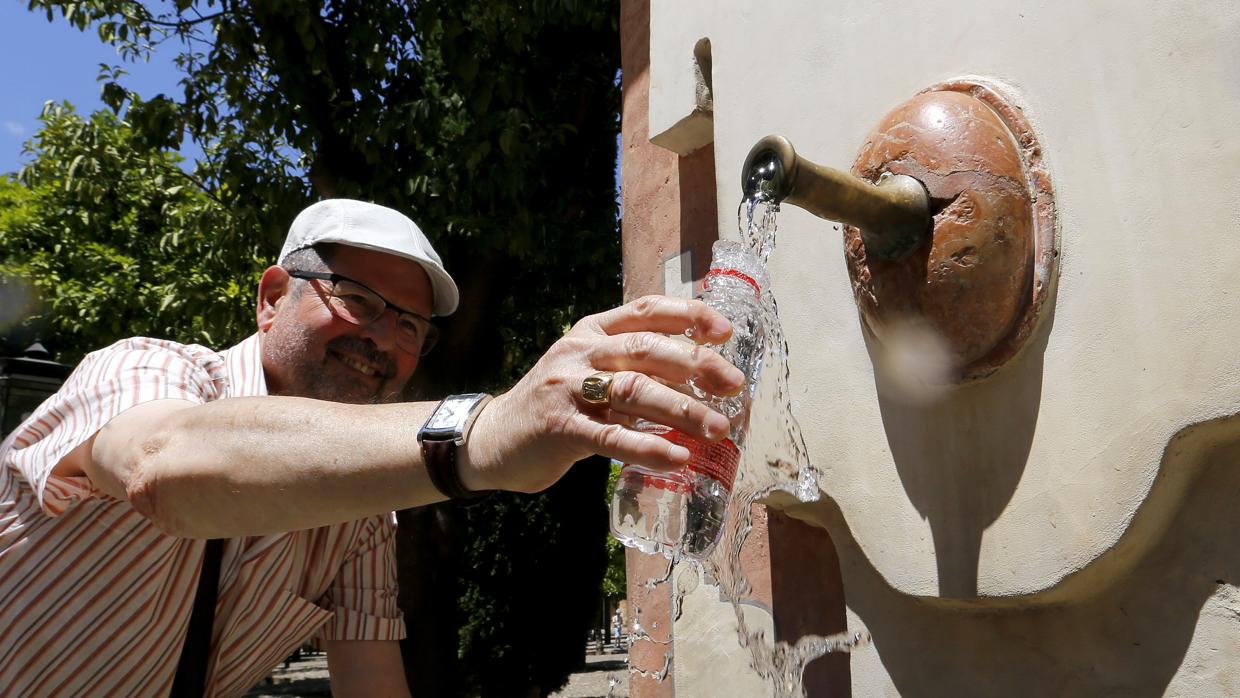 Un hombre llena una botella de agua en una fuente del Patio de los Naranjos