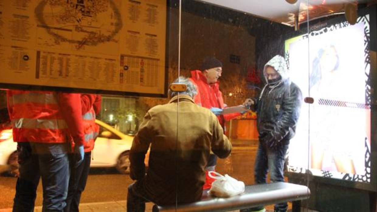 Personal de la Cruz Roja asiste a dos hombres sin recursos en una parada de autobús