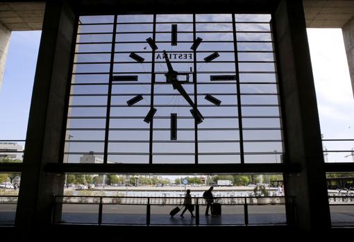 Dos viajeros pasan por debajo del reloj de la estación