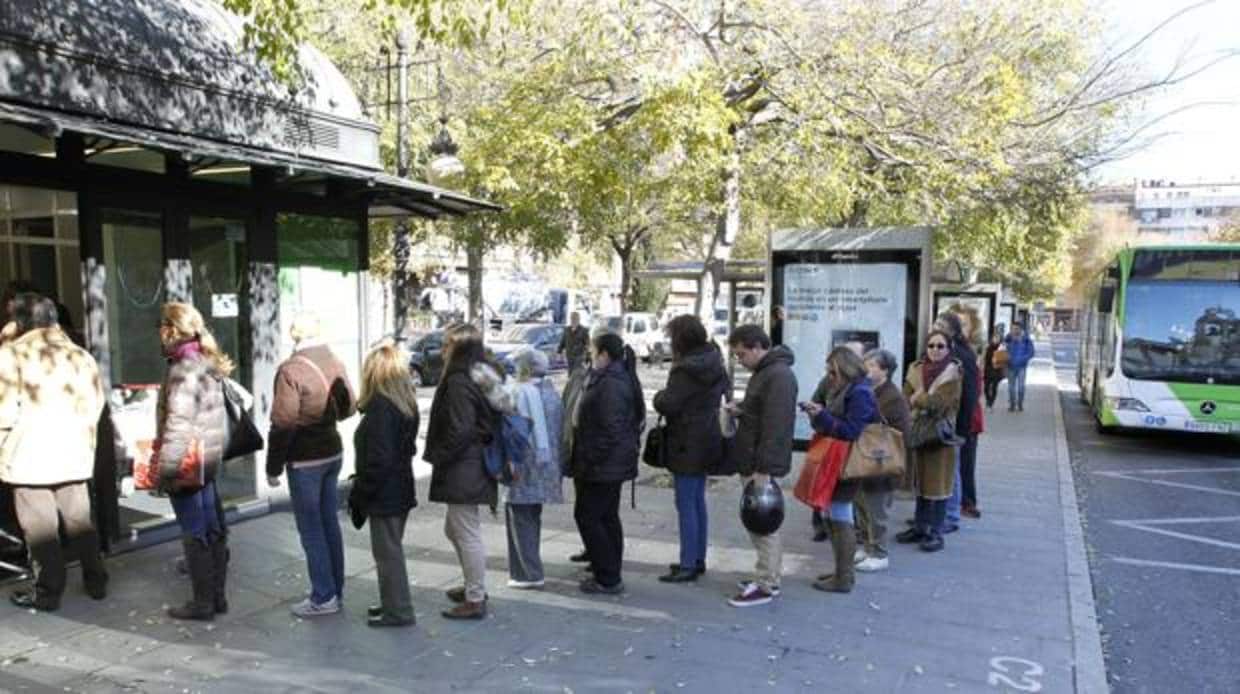 Varias personas hacen cola para adquirir su bono del autobús en la plaza de Colón