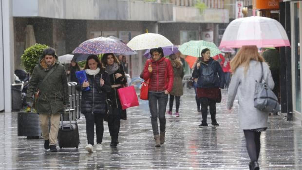 Varias personas pasean por el Centro de Córdoba con paraguas, este domingo