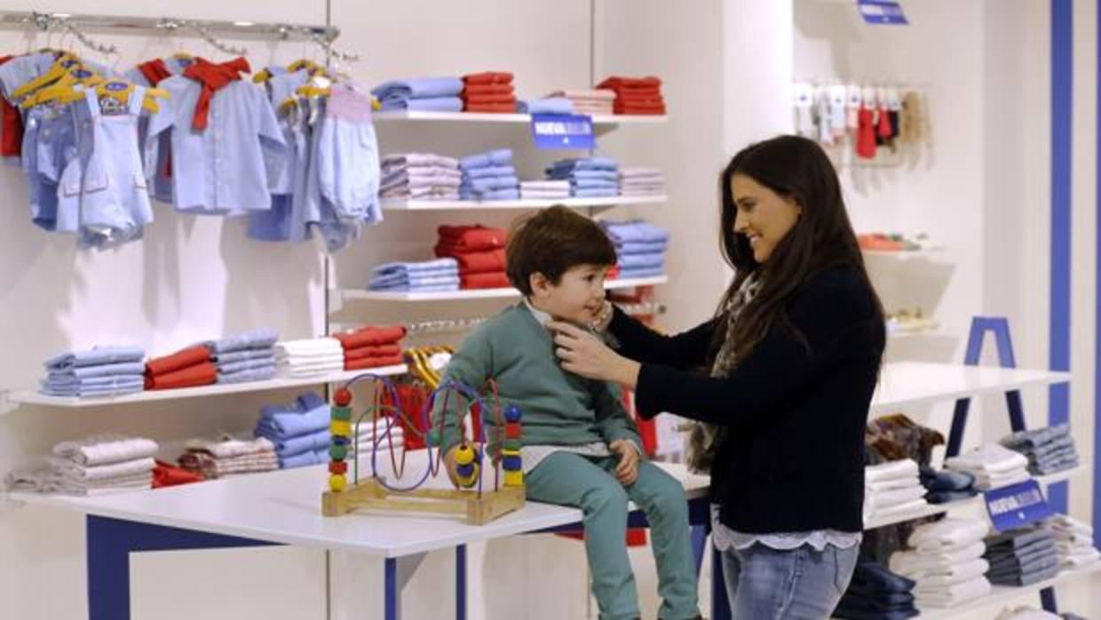 Una mujer le prueba ropa a un niño en una tienda de moda infantil