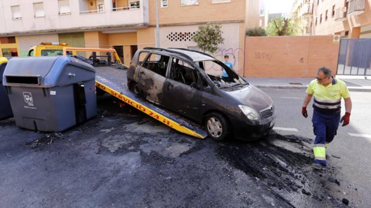 Un operario retira un coche quemado junto a un contenedor