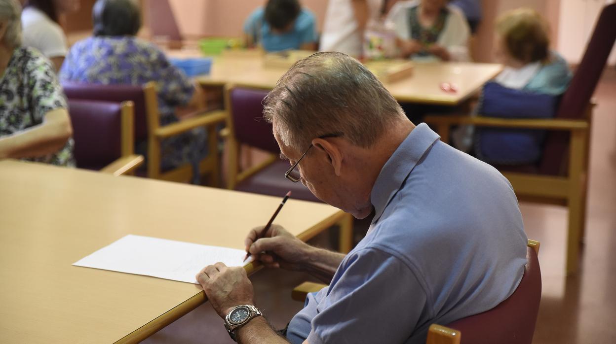 Un hombre con alzheimer escribe en un papel en un centro para personas con este tipo de problemas