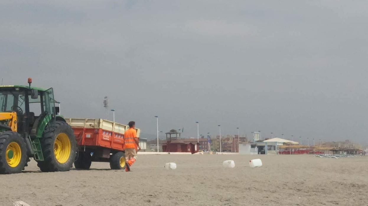 Un operario de limpieza se dispone a recoger algunos de los bidones abandonados en la playa.