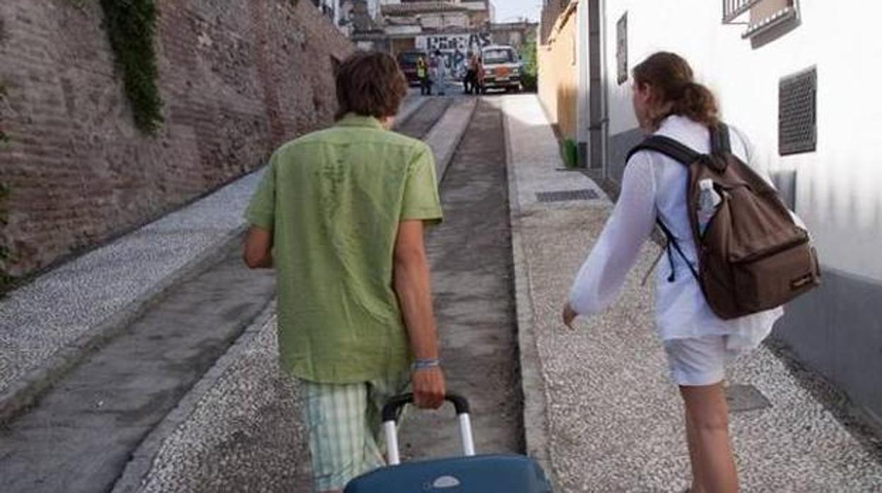 Dos turistas caminan con sus maletas por el Albaicín de Granada.