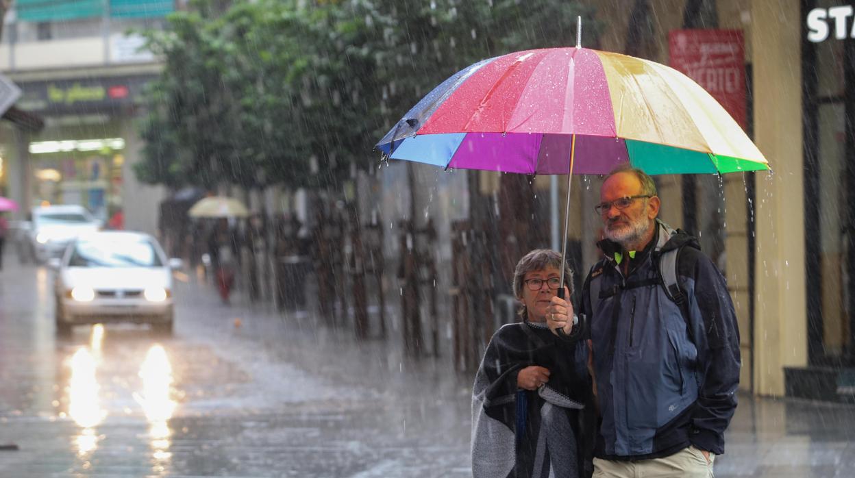 Una pareja se refugia en un paraguas en plena lluvia en Las Tendillas