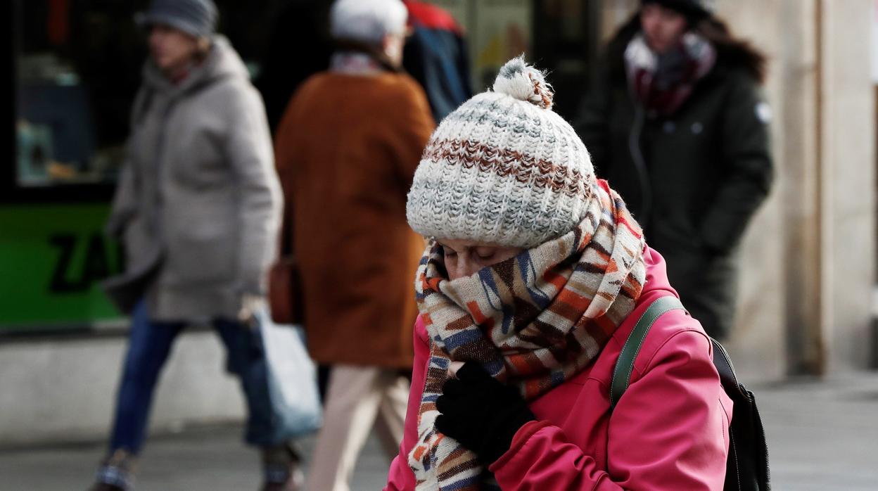 Una mujer se abriga contra el frío en una calle comercial
