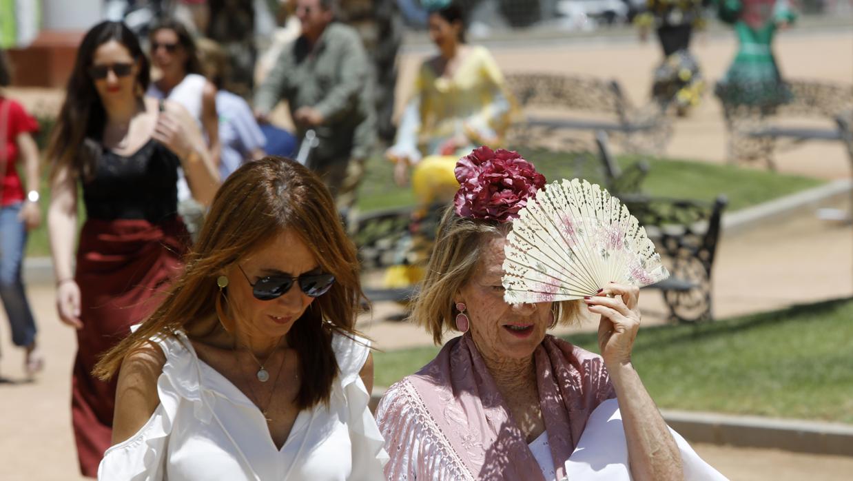 Dos mujeres pasean por la feria tapándose el sol con un abanico