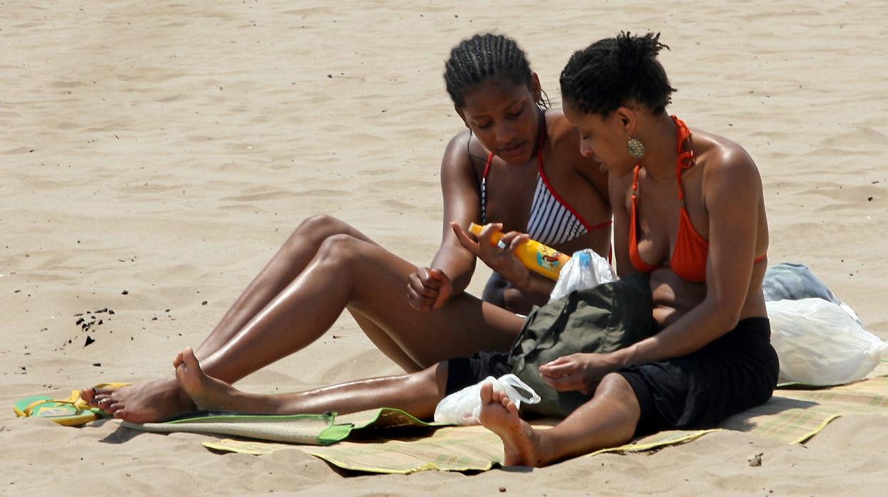 Dos mujeres en una playa española con un frasco de protector solar