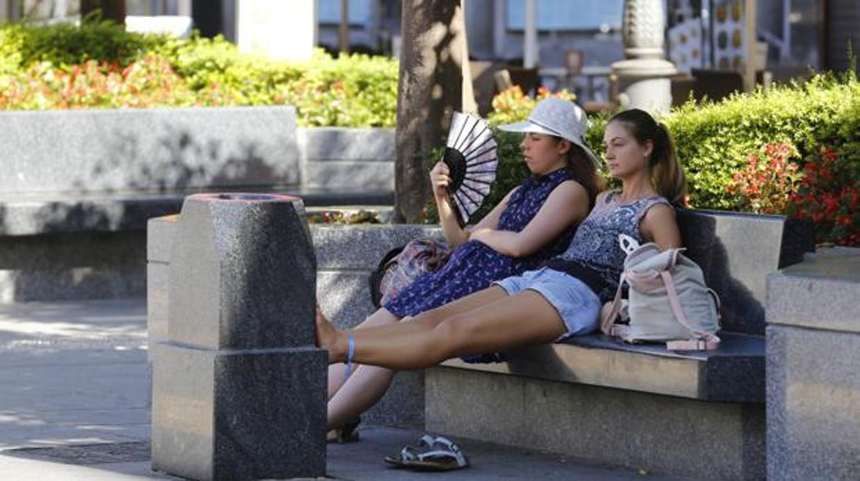 Dos jóvenes se refrescan con un abanico en las Tendillas