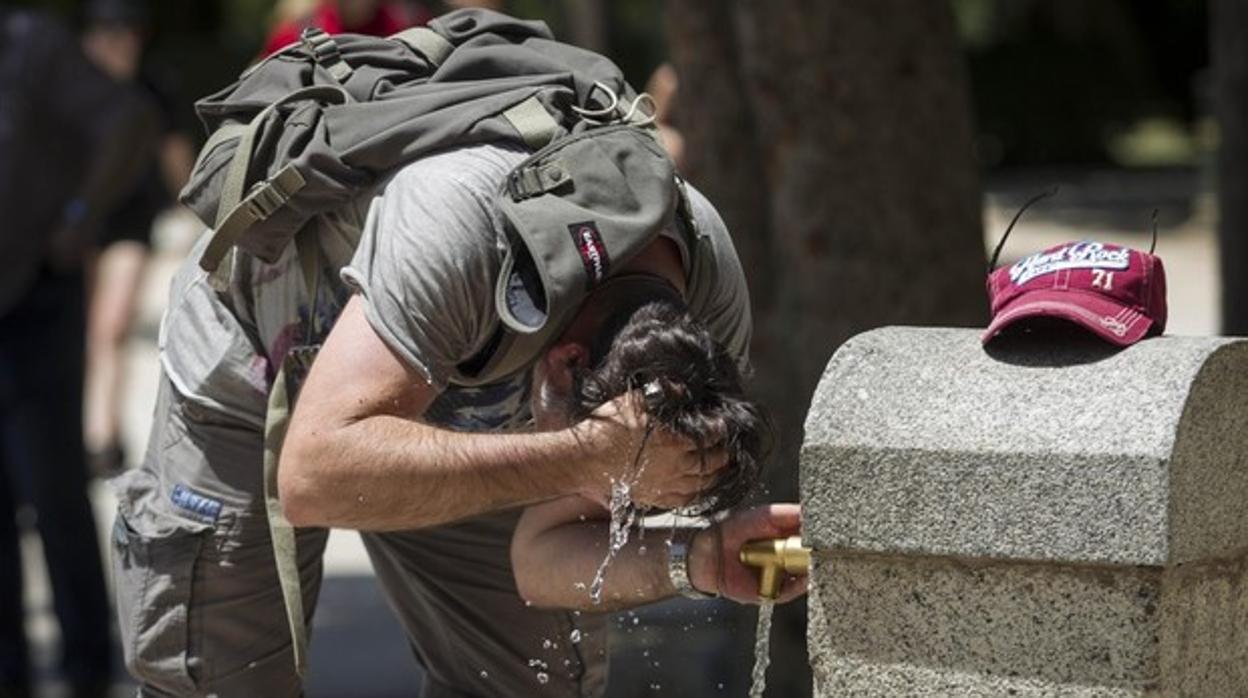 Un hombre se refresca en una fuente de un parque