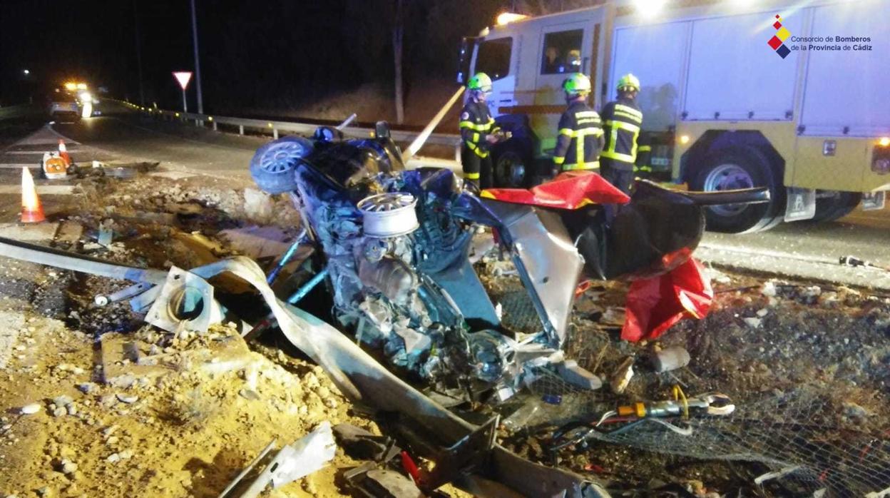 Los bomberos, junto al coche siniestrado, que ha quedado completamente destrozado