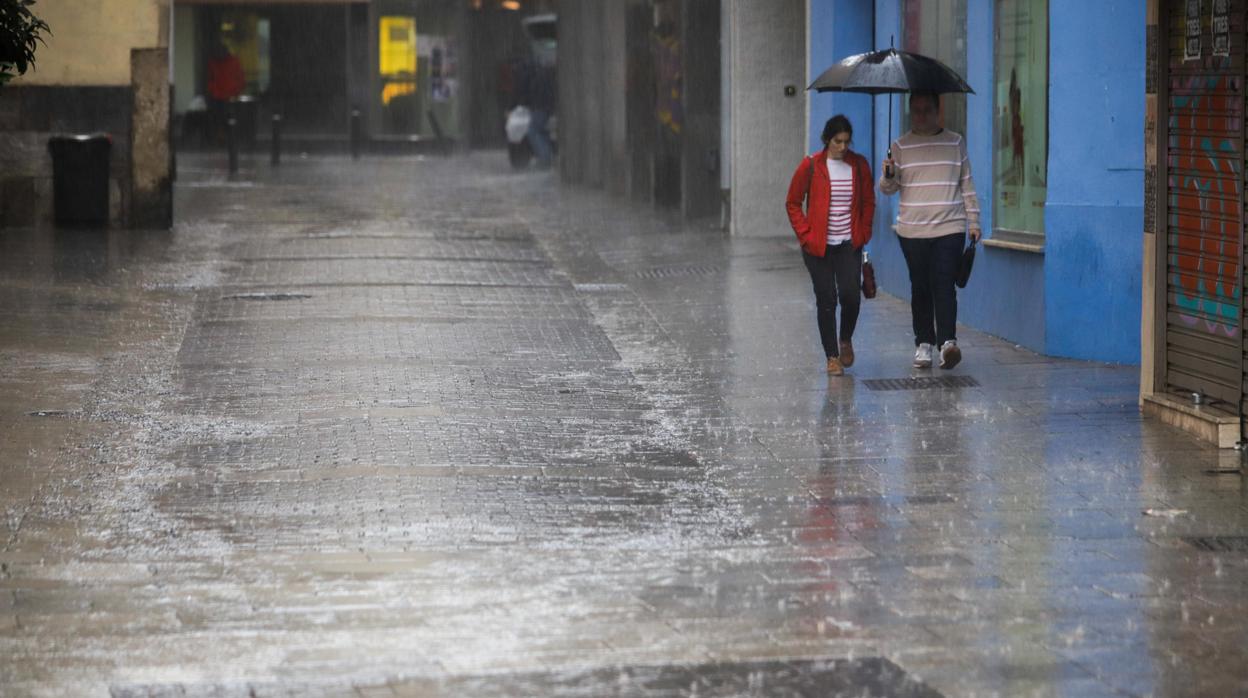 Dos jóvenes caminan bajo la lluvia por una calle del centro