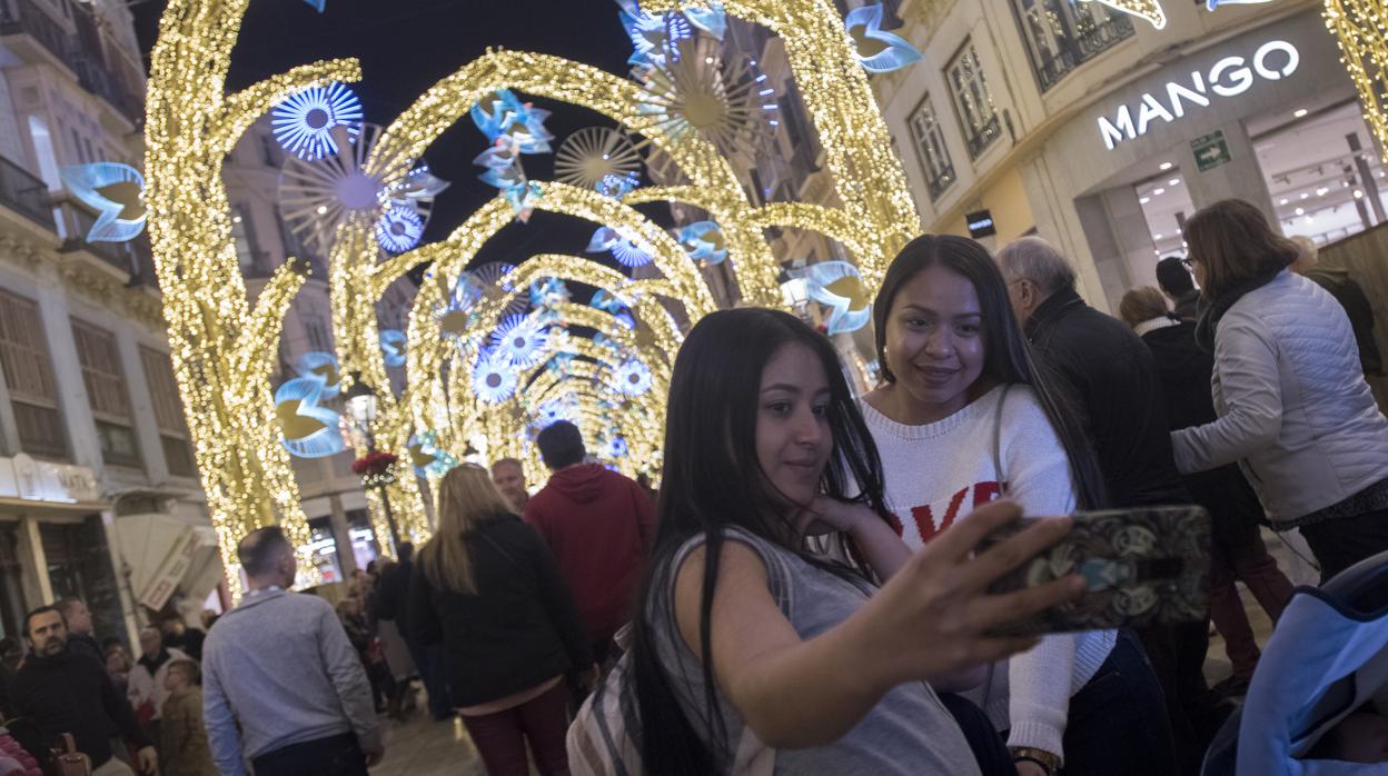 Dos jóvenes se fotografían bajo el "bosque" navideño de calle Larios