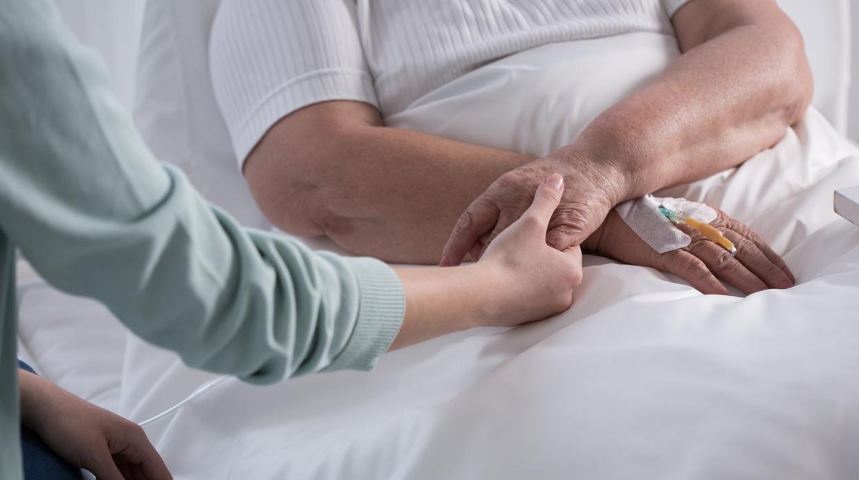 Una mujer sostiene la mano de una anciana ingresada en un hospital