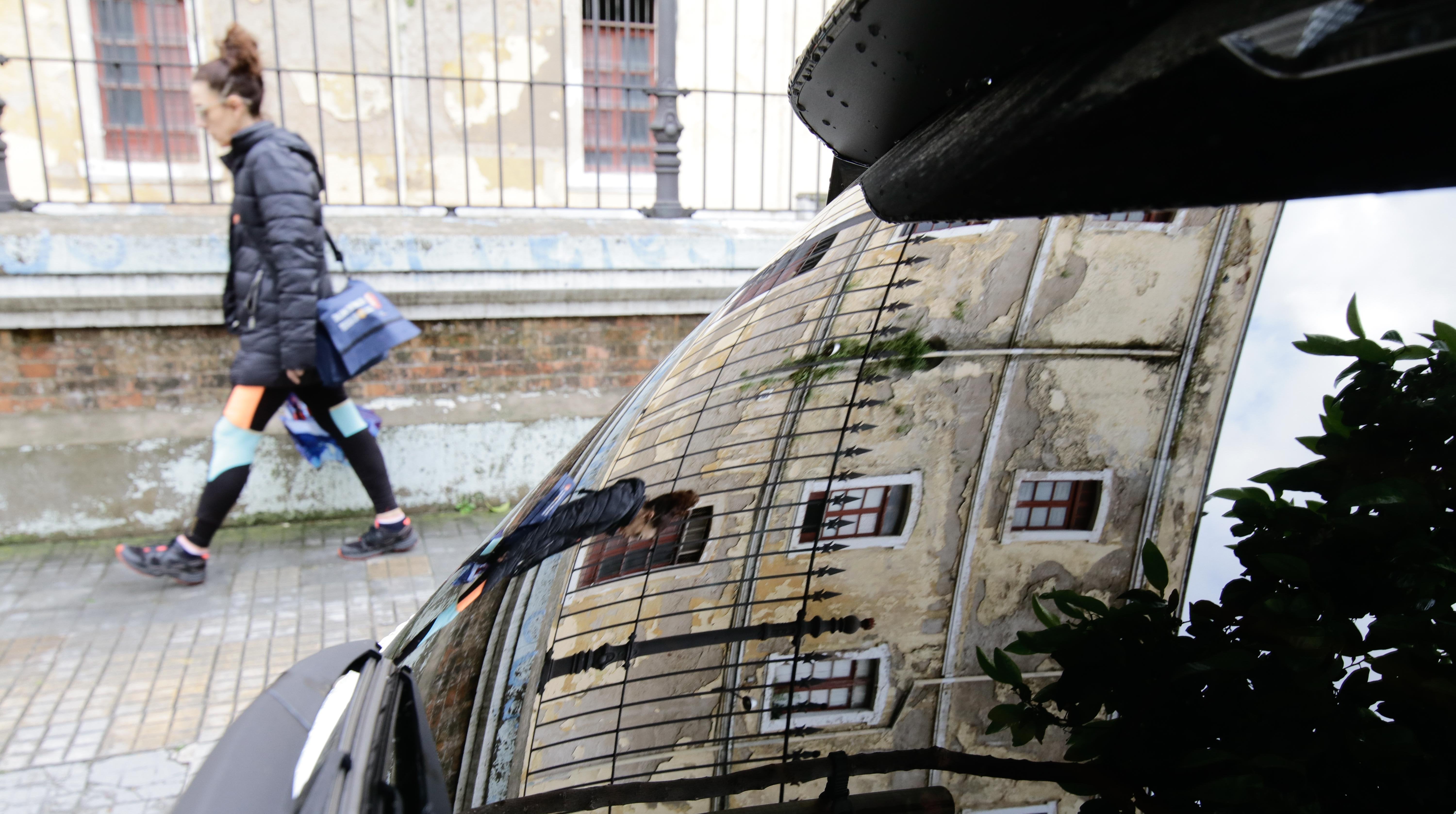 Una joven pasa por delante de la Zona Militar, reflejada en la luna de un coche