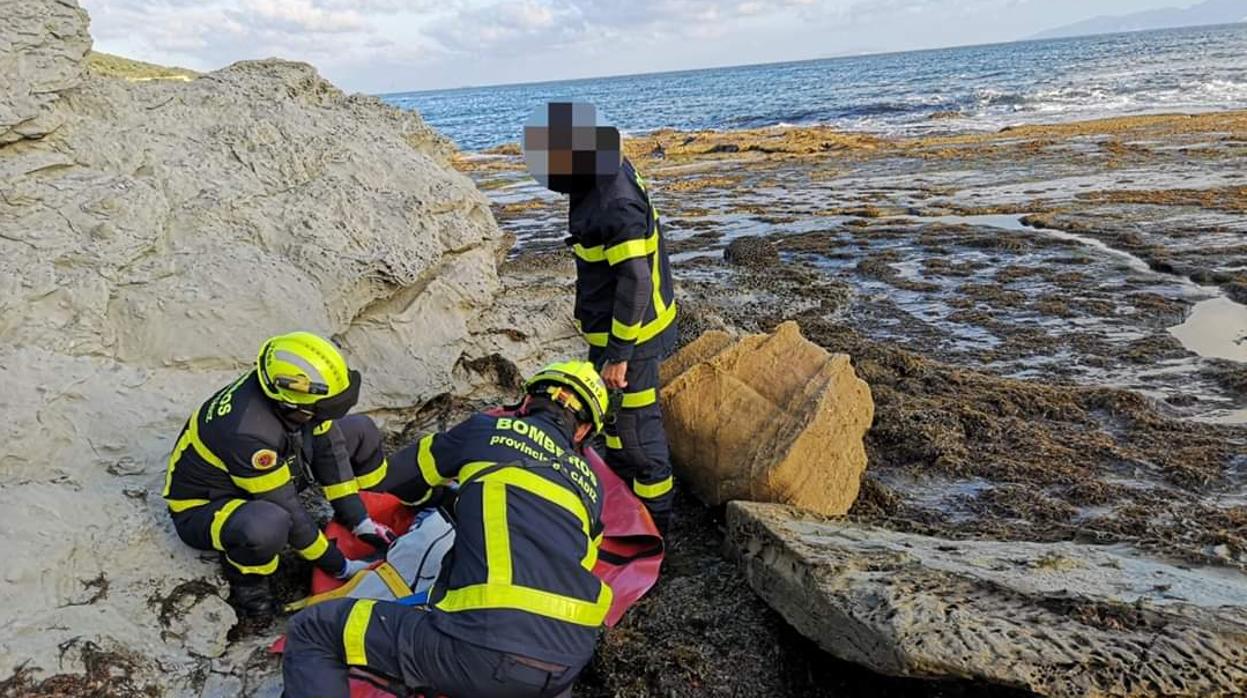 Los bomberos atienden a la víctima que cayó en esta zona rocosa de la costa de Algeciras